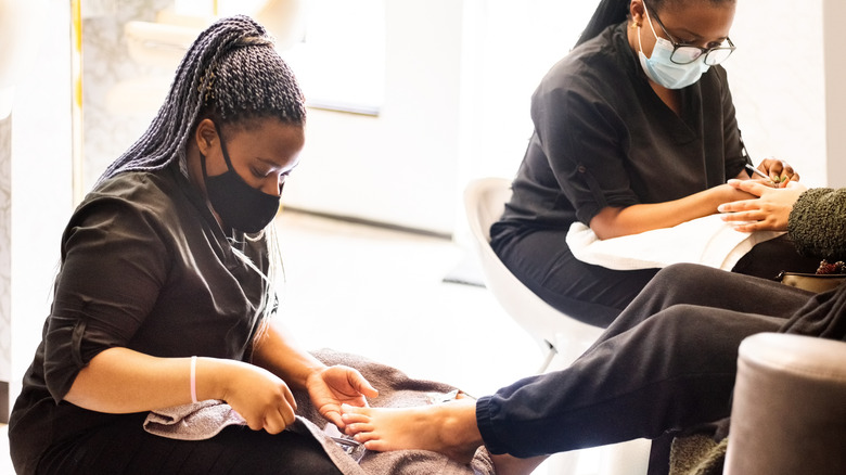Manicurist in black scrubs working on clients feet