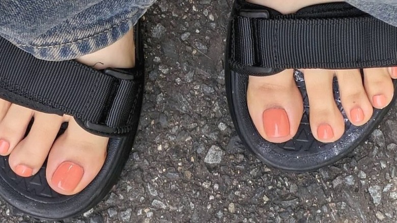 A woman wearing black sandals that show her milky peach manicure
