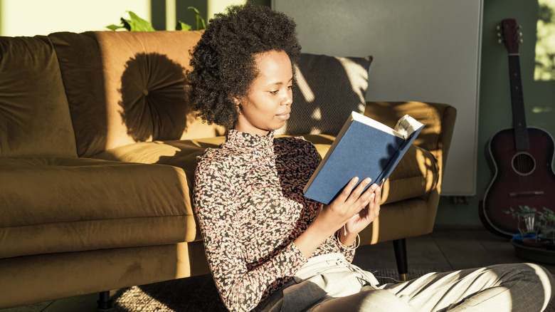 Woman leaning back on her couch and reading a book