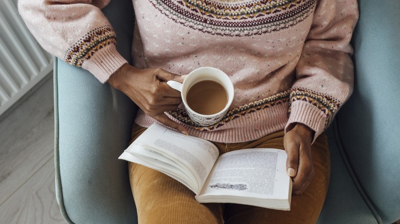 A woman's holding a hot drink while reading a book