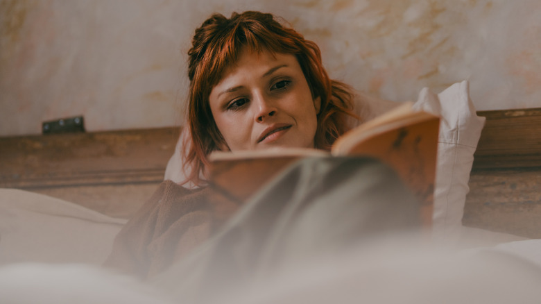 Dark-haired woman reading book in bed