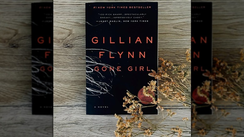 A copy of the novel "Gone Girl" on a wooden table with some dried flowers