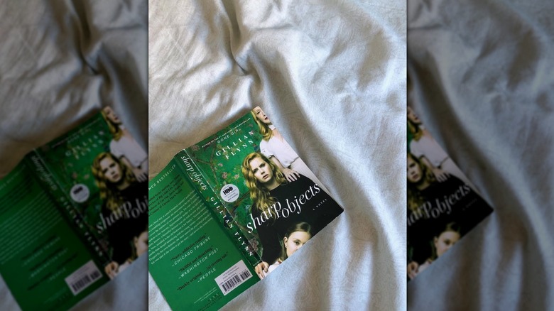 A copy of the novel "Sharp Objects" lying open and face down on a white sheet