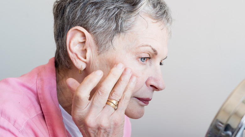Older woman examining her face in a mirror