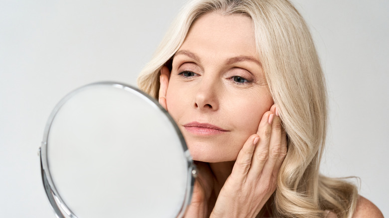 A mature woman examining her skin in a mirror