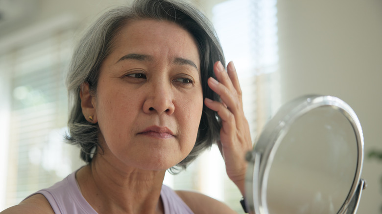 A mature woman examining her skin in a mirror