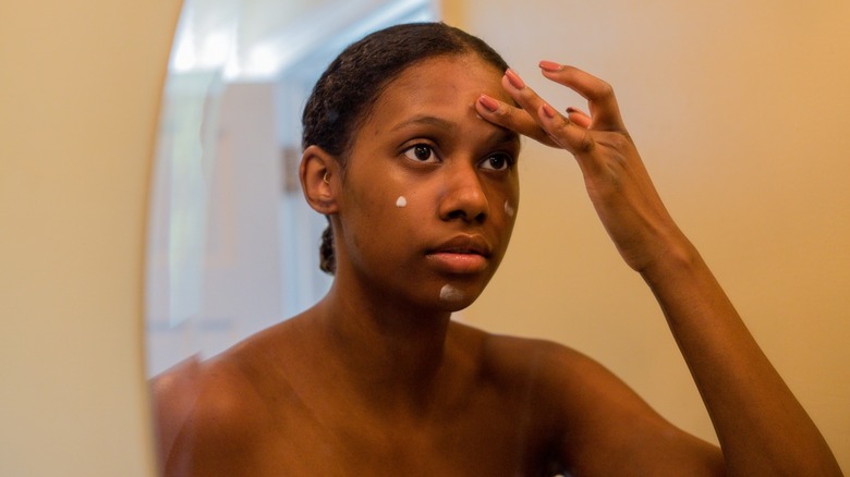 A woman looking in the mirror while applying face primer