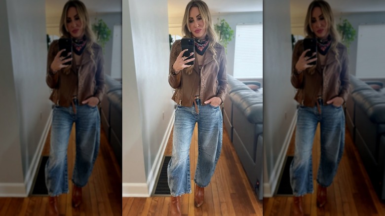 A woman wearing barrel jeans and ankle boots, posing for a selfie in front of a black couch