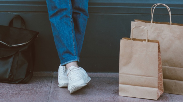 A woman wearing lowkey sneakers with stovepipe jeans while standing beside shopping bags