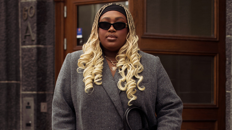 A woman with blonde braided curls and a black headband with a grey blazer