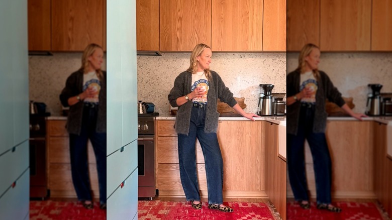 A woman standing in a kitchen wearing dark wash jeans and a cardigan