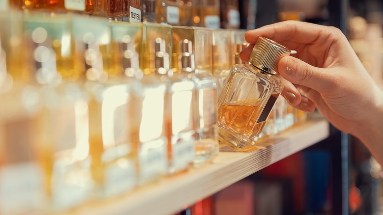 A woman's hand taking perfume off the shelf in a store