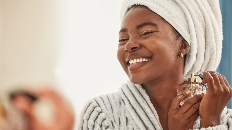A smiling woman spraying perfume onto her neck
