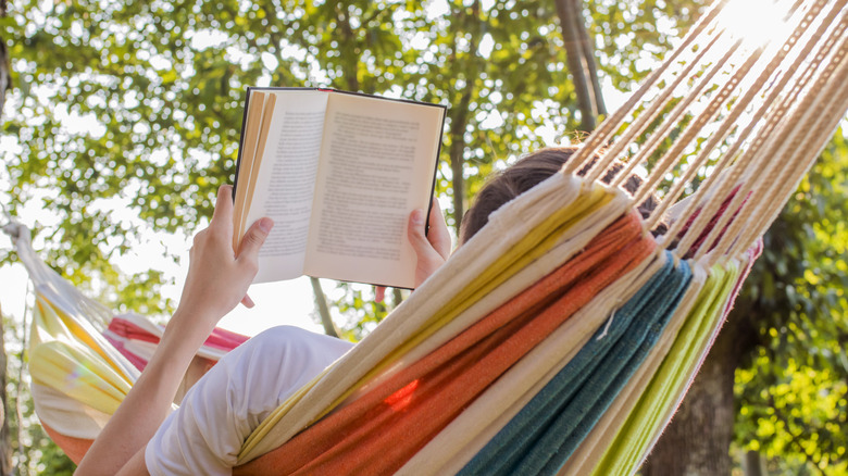 Snapshot of unseen person reading an open book in a rainbow-colored hammock on a sunny day