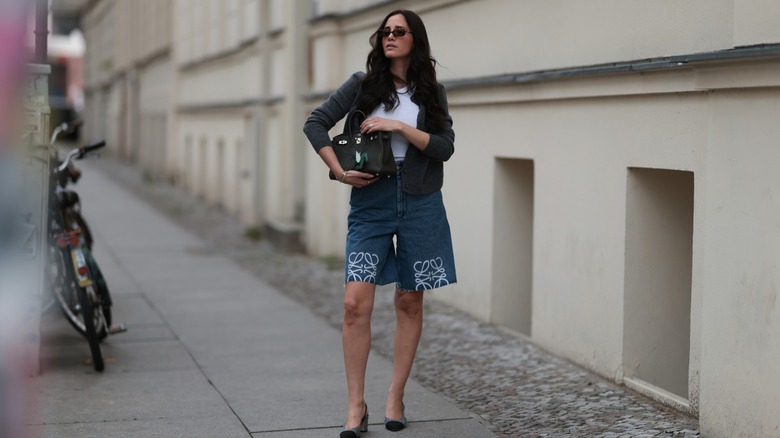 A woman wearing long denim shorts with a white top and jacket
