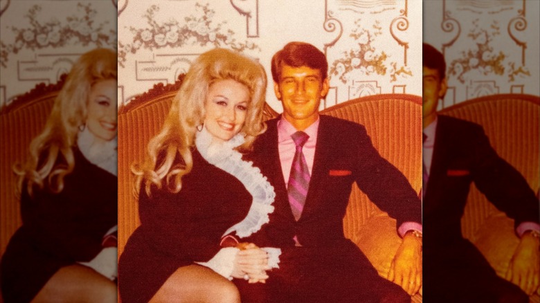Retro snapshot of Dolly Parton sitting with her husband Carl Dean on a couch as they smile into the camera