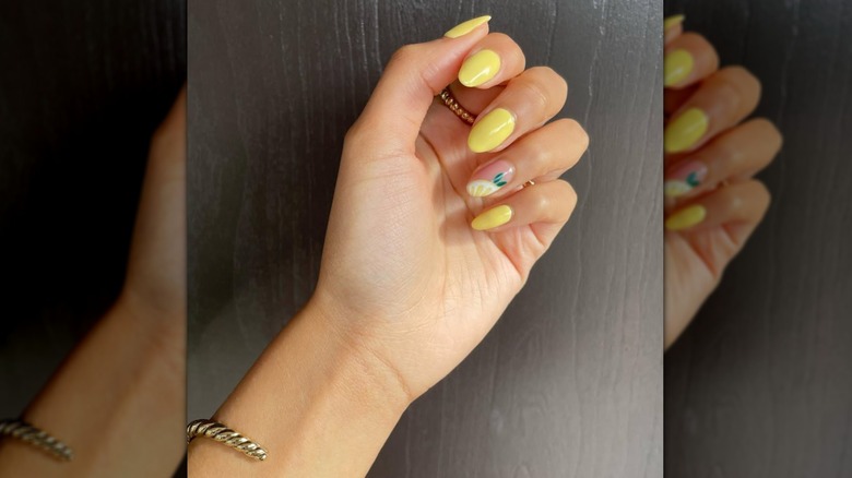 A close up of a woman with yellow nails with lemon detailing on her fourth finger
