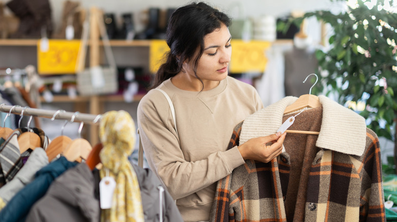 A woman in a store checking the price tag on a coat next to a rack of coats