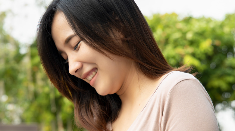 A woman smiles and pinches the fat around her chin.