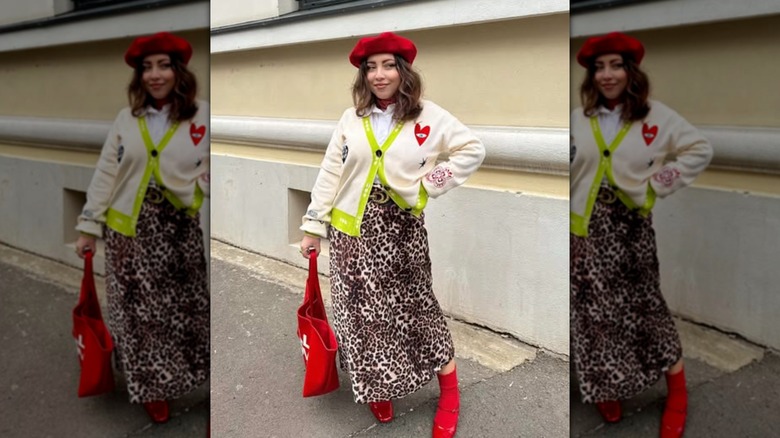A woman wearing a cheetah skirt and white sweater with pops of red accessories