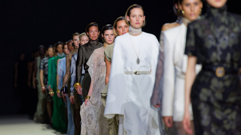 A line of runway models all wearing different colors