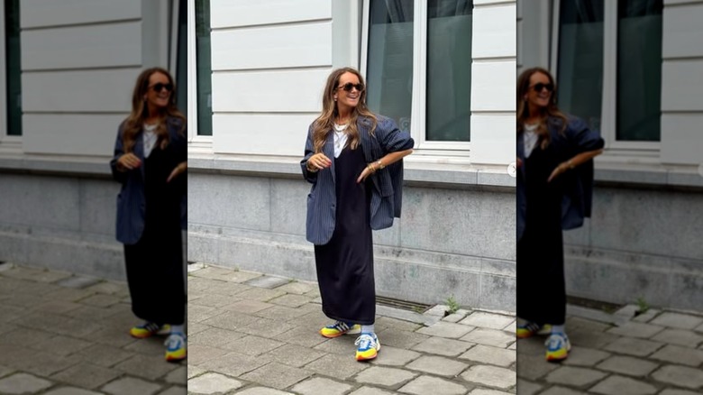 A woman standing on the steet wearing a navy blue dress and blazer with  neon shoes