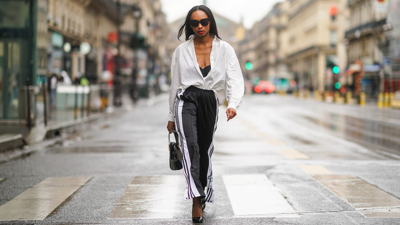 A woman with black track pants and a white blouse walking down the street