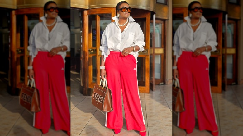 A woman in red track pants and a white blouse with a big pearl necklace
