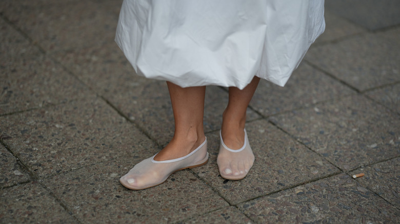 A close up of a woman in white mesh ballet flats with a white skirt