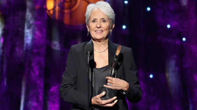 Joan Baez holding her Rock and Roll Hall of Fame Induction award in 2017 while wearing a black outfit