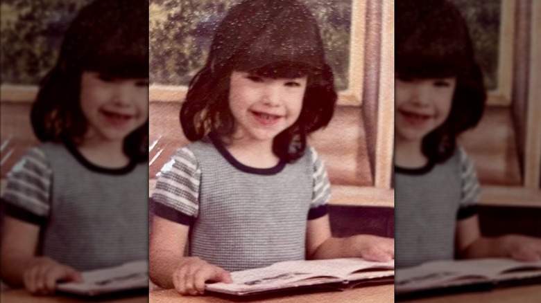Young Lauren Sánchez Bezos sitting at a school desk with a book