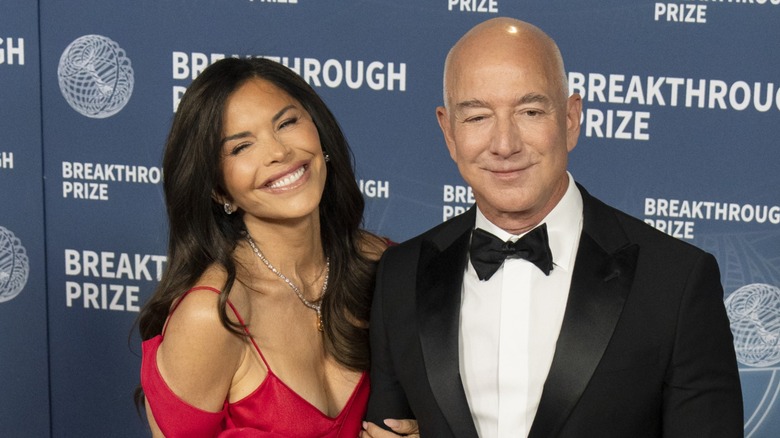 Lauren Sánchez Bezos smiling and holding onto the arm of Jeff Bezos on the red carpet in 2025