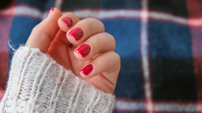 Close-up of partially closed hand with candy apple red nail polish against an out-of-focused flannel background
