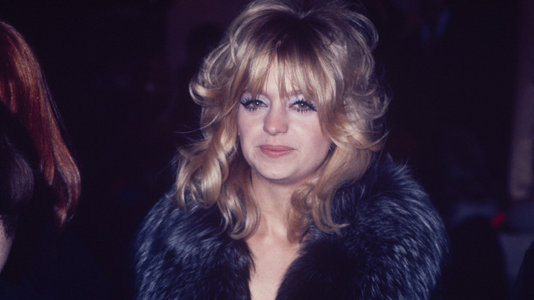 Goldie Hawn smiles wearing a fur-trimmed black coat