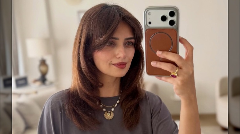 A woman taking a selfie in a mirror with hair containing face faming layers