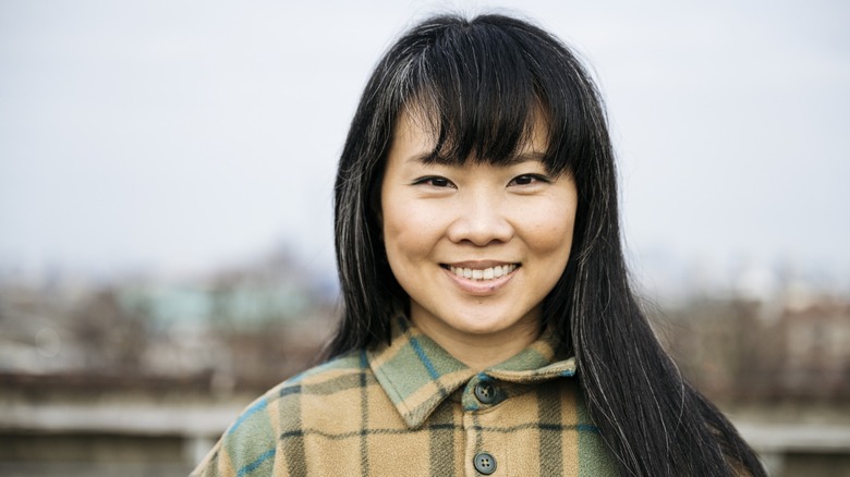 A women with graying hair and bangs in a plaid coat smiling while outside
