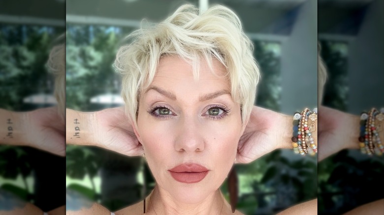 A woman posing with her hands behind her head and a blond pixie cut
