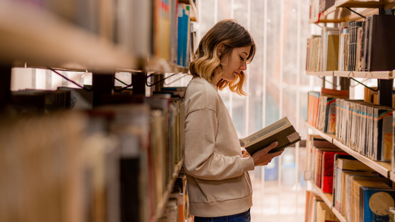 Young woman reading book in between book shelves