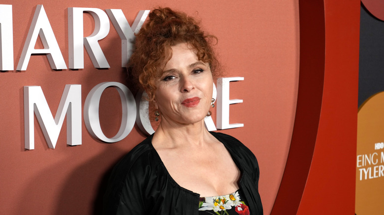 Bernadette Peters smiling on the red carpet in 2023 wearing a black floral dress with a black jacket.