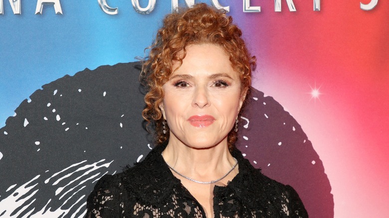 Bernadette Peters posing on the red carpet in front of a red and blue background.