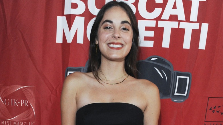 Kristen Vaganos flashing a big smile on the red carpet in 2023 while standing in front of a red background