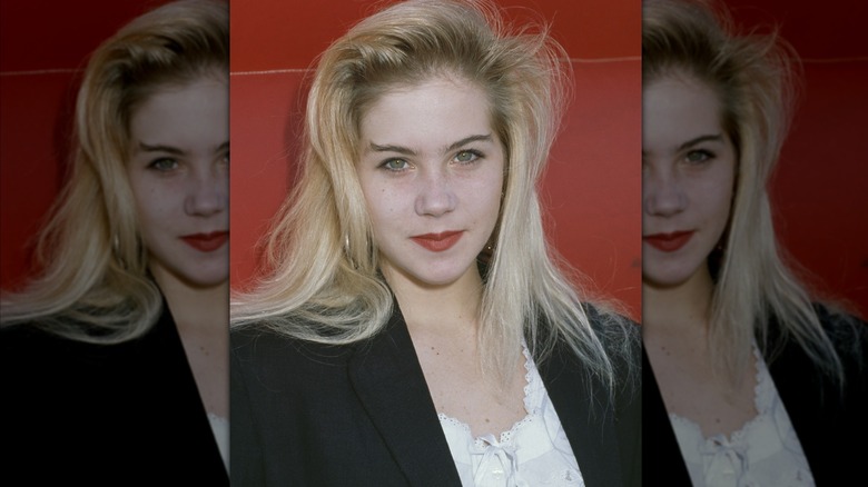 Christina Applegate posing in a blazer in front of a red background in 1988