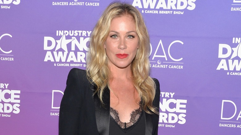 Christina Applegate on the red carpet in 2017 wearing red lipstick in front of a purple background