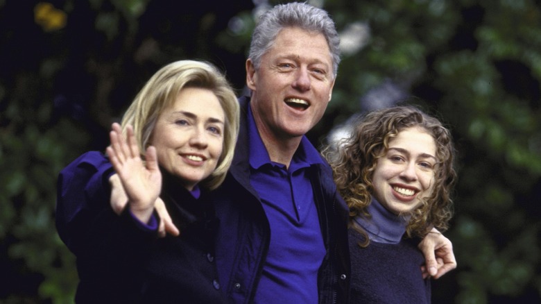 Bill Clinton with his arms around a waving Hillary Clinton and a young Chelsea Clinton in 1997