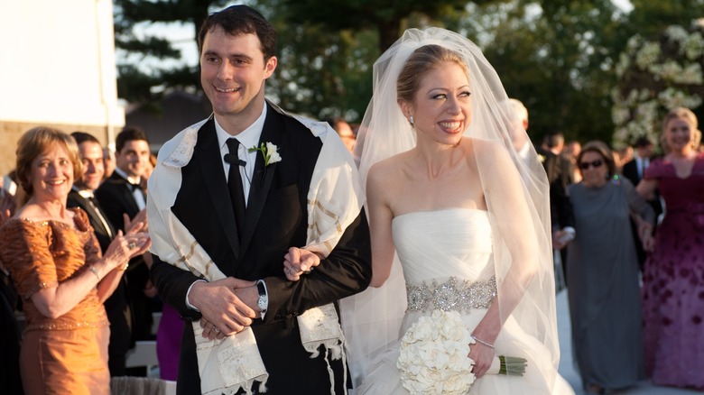 Marc Mezvinsky and Chelsea Clinton linking arms on their wedding day while guests look on
