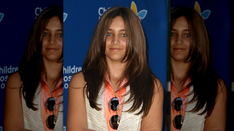 Paris Jackson slightly smiling at an event in 2011, standing in front of a blue background