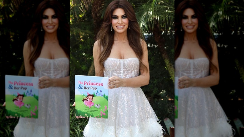 Kimberly Guilfoyle holding up a kids book while wearing a white dress