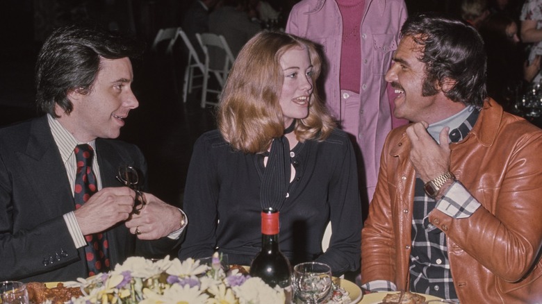 Peter Bogdanovich, Cybill Shepherd, and Burt Reynolds sitting at a table in 1971
