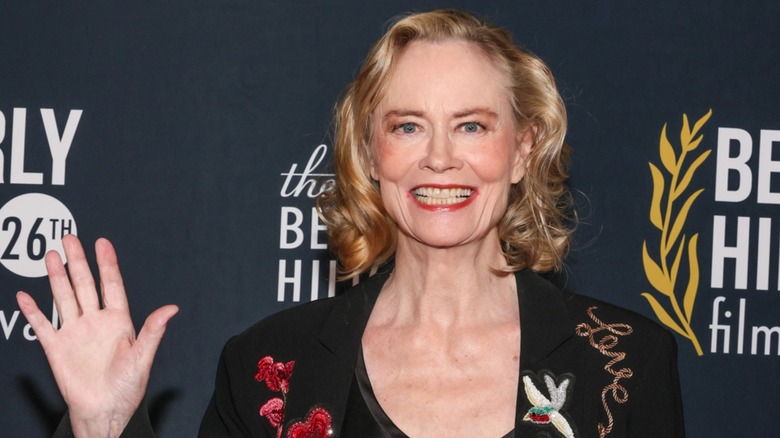 Cybill Shepherd waving on the red carpet in front of a black background in 2026