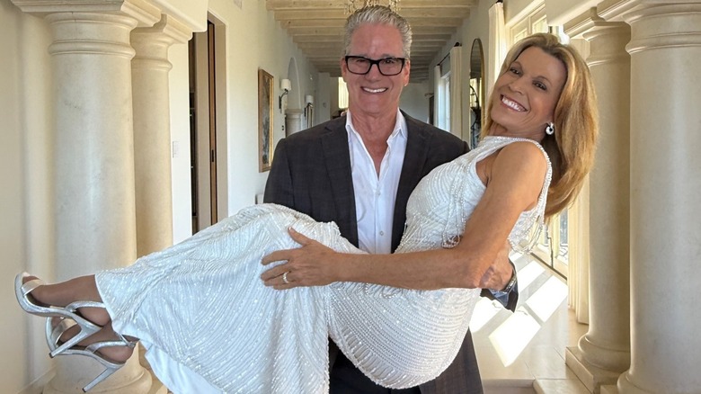 John Donaldson, wearing a suit, holding Vanna White in a beaded white dress